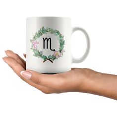 a woman's hand holding a coffee mug with the letter m in floral wreath