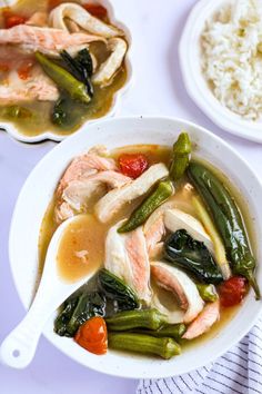 two bowls filled with soup and vegetables next to rice on a white tablecloth covered table