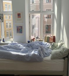 an unmade bed sitting in front of two windows