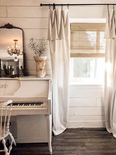 a white piano sitting in front of a window next to a mirror and table with a vase on it