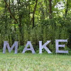 the word make is made out of metal letters in front of some bushes and trees