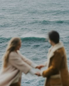 two people holding hands while standing in front of the ocean