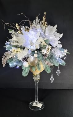 a glass vase filled with white flowers and greenery on top of a table next to a black wall