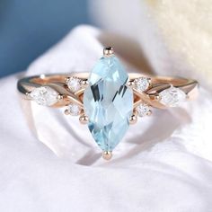 a ring with an aqua blue topazte and white diamonds on the side, sitting on a cloth