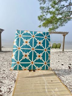 a blue and white quilt sitting on top of a wooden walkway next to the ocean