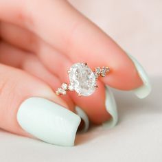 a woman's hand holding a ring with a diamond on it and white nails