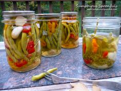 several jars filled with pickles and peppers sitting on a table next to a pair of scissors