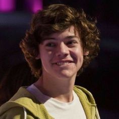 a young man with curly hair smiles at the camera while wearing a yellow hoodie