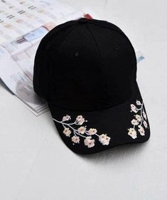 a baseball cap with embroidered flowers on it next to a cell phone and pen sitting on a table