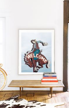 a welcome sign hangs on the wall above a coffee table with books and a bicycle