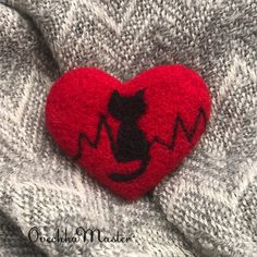 a red heart with a black cat on it sitting on top of a gray sweater