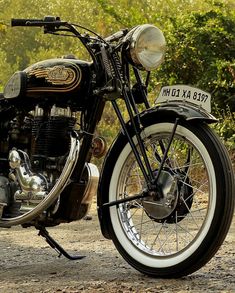 a motorcycle parked on the side of a dirt road next to some bushes and trees