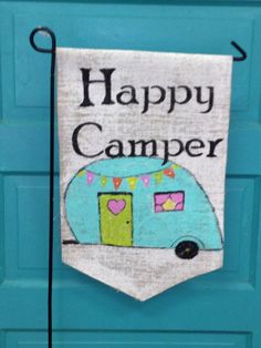 a sign that says happy camper hanging on a blue door with a black hook