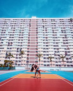 two women are playing tennis in front of a high rise apartment building on a sunny day