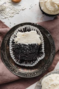 a chocolate cupcake with white frosting on a plate next to other cupcakes