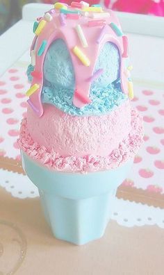 an ice cream cone with pink, blue and yellow frosting on top sitting on a table