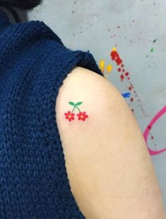 a woman with a small tattoo on her arm that has red flowers and leaves painted on it