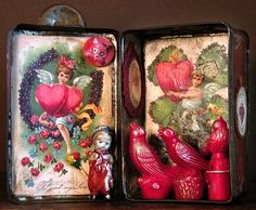 an open tin box with two red birds in front of it on a wooden table