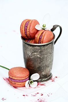 a metal cup filled with pink macaroons next to a white and green flower