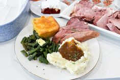 a white plate topped with meat and mashed potatoes next to green beans, asparagus and other foods