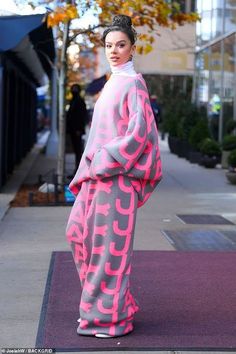 a woman is standing on the sidewalk wearing a pink and grey sweater with black letters