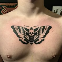 a man's chest with a moth tattoo on it and a skull in the middle