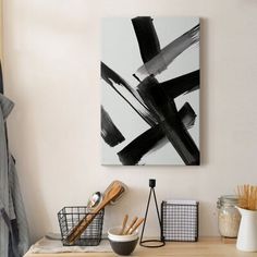 an abstract painting hangs on the wall above a wooden table with bowls and utensils