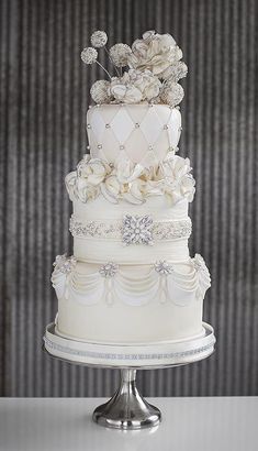 a three tiered white wedding cake with flowers on the top and sides, sitting on a silver pedestal