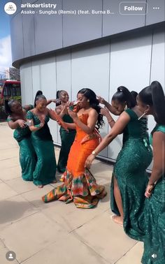 a group of women in green dresses dancing on the sidewalk with their arms around each other