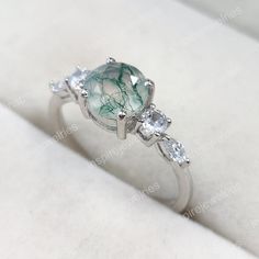 a ring with green and white stones in it on a white cloth covered tablecloth