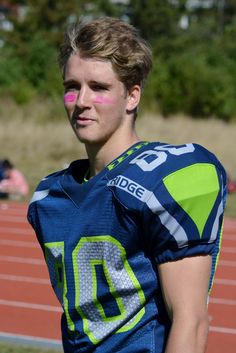 a young man wearing a football uniform with pink eyeliners on his face and in the background is a running track