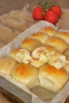 some rolls are sitting in a pan on a table next to tomatoes and a tomato