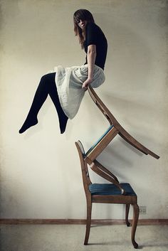 a woman sitting on top of a wooden chair with her legs up in the air