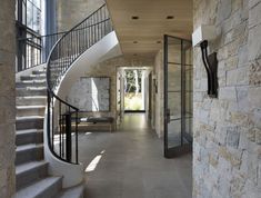 a long hallway with stone walls and stairs leading to the second floor, along with a glass door that leads to another room