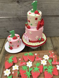 a cake and some decorated cookies on a wooden table next to a plate with strawberries