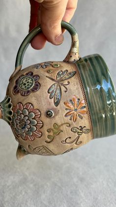 a hand holding a teapot with flowers painted on the outside and inside it's handle