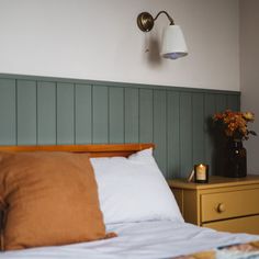 a bed with white sheets and pillows next to a lamp on the wall above it