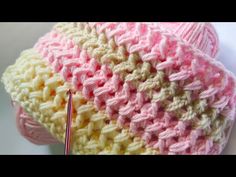 a crocheted pink and white hat with a knitting needle in the center, on top of a white surface