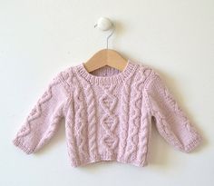 a pink knitted sweater hanging on a white wall next to a wooden hanger