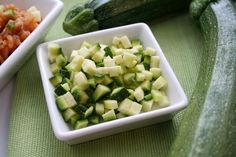 a white bowl filled with sliced up cucumbers and broccoli on top of a green table cloth