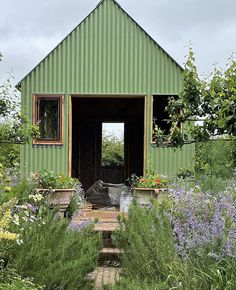 a green building surrounded by lots of plants and flowers