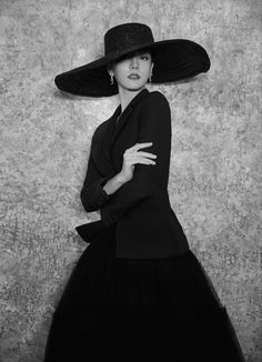 a woman in a black dress and large hat poses for a photo with her hands on her hips