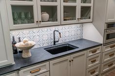 a kitchen with white cabinets and black counter tops, including a sink in the center