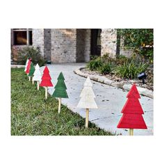 wooden christmas trees are lined up on the sidewalk in front of a brick house and driveway