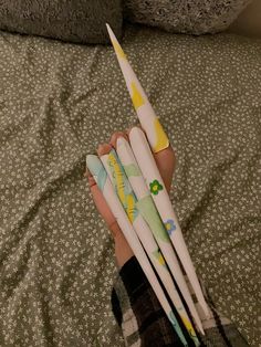 a person holding four toothbrushes in their hand on top of a bed next to a pillow