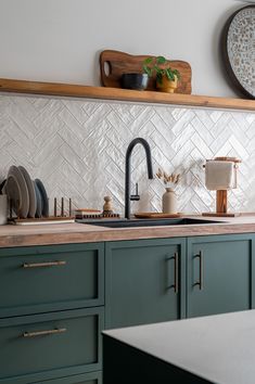 a kitchen with green cabinets and white tile backsplashing, wooden shelves above the sink