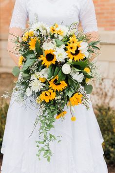 a bride holding a bouquet of sunflowers and greenery