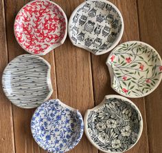 six bowls are arranged in a circle on a wooden surface, each with different designs