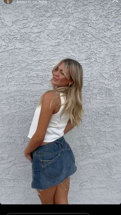 a woman standing in front of a wall with her back to the camera and wearing a denim skirt