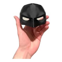 a hand holding up a black mask with white eyes